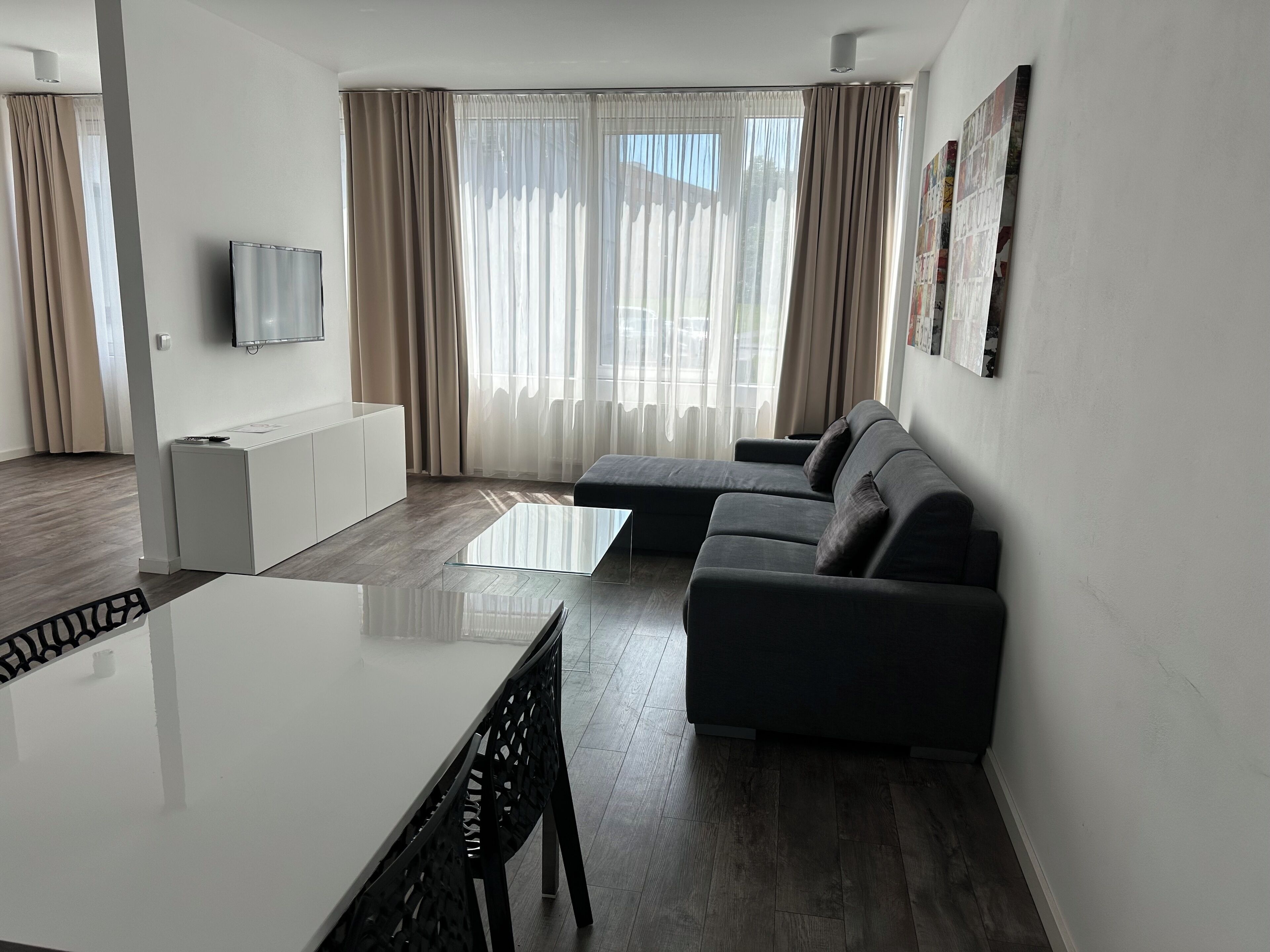 A modern living room with a glass coffee table, a grey sofa, and a white TV stand.