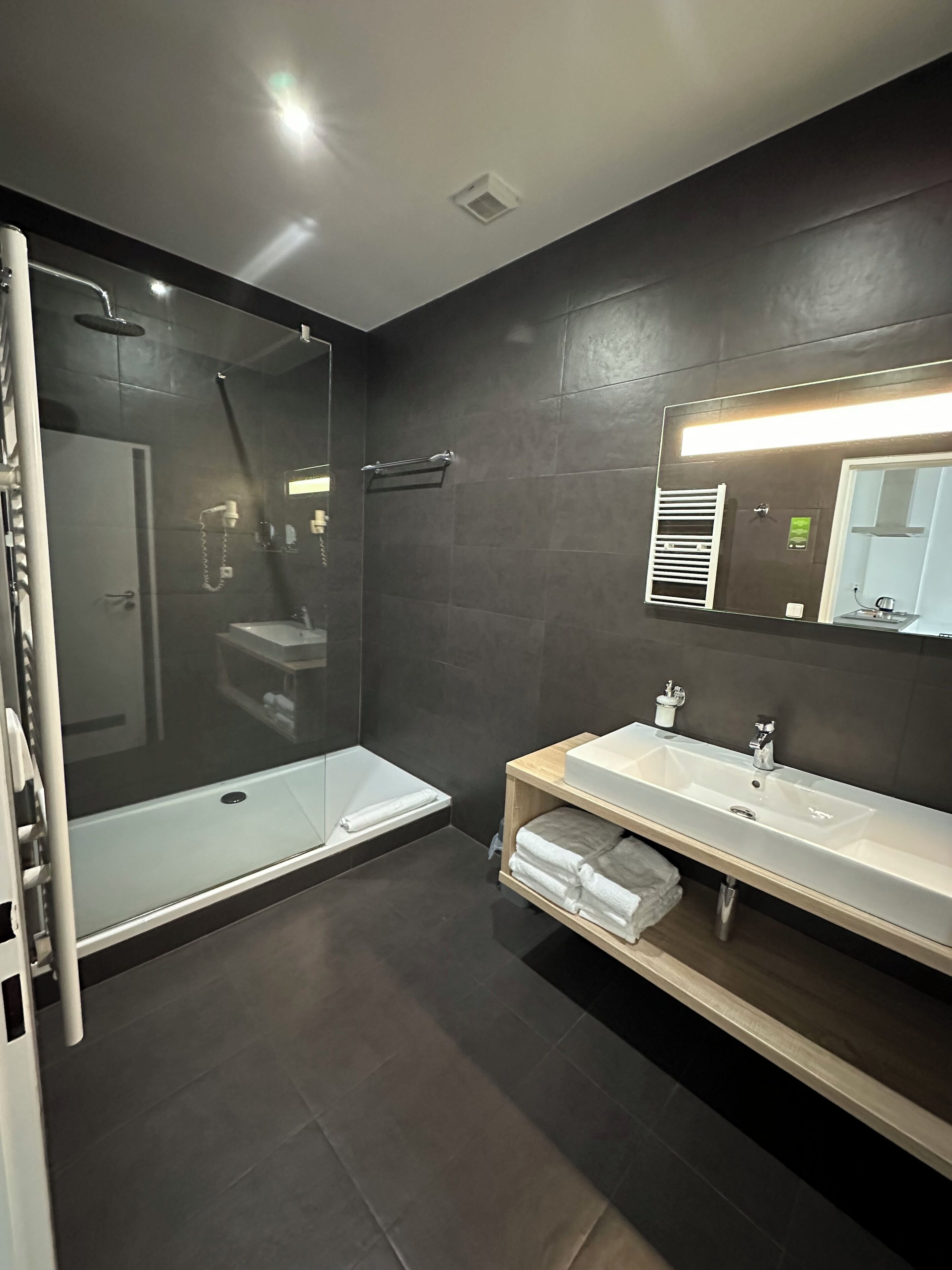 Un baño moderno con ducha envuelta en vidrio, tocador con espejo y un perchero para toallas.