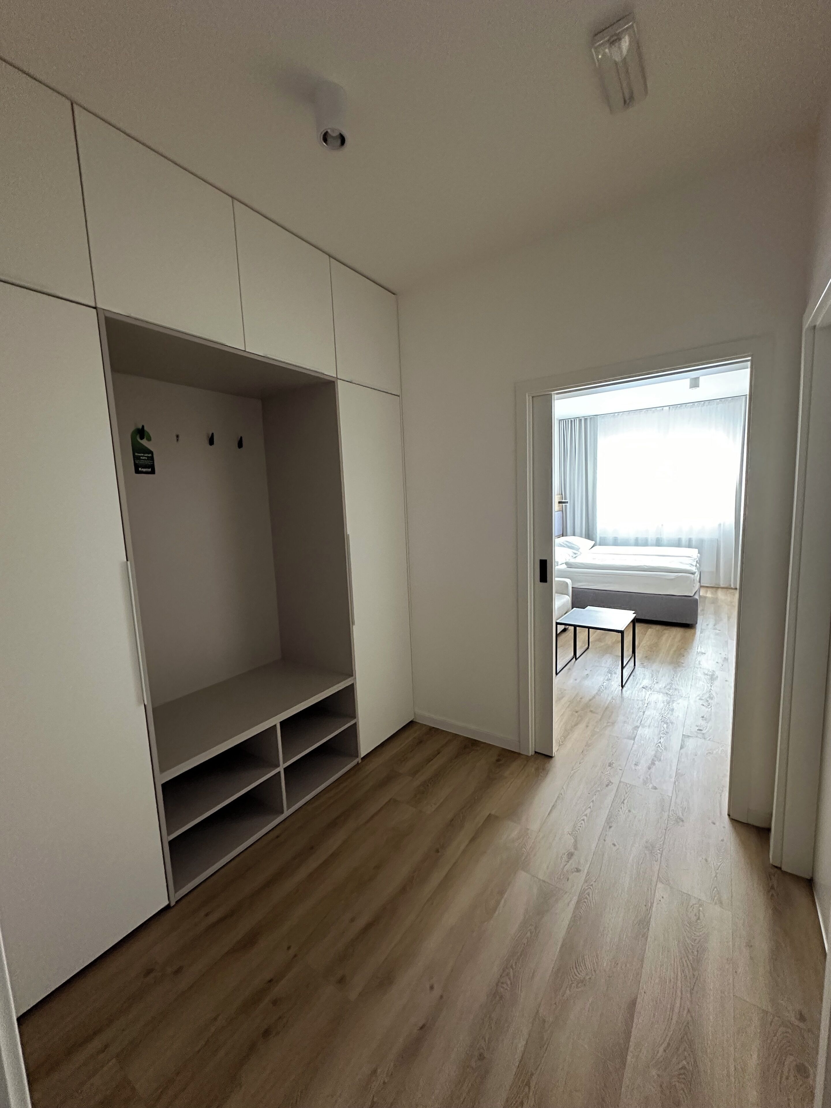 Una habitación con un vestidor amplio, una cama con cabecera blanca y una mesita pequeña.