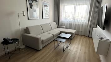 A modern living room with a sofa, two coffee tables, a flat-screen TV, and artwork on the wall.