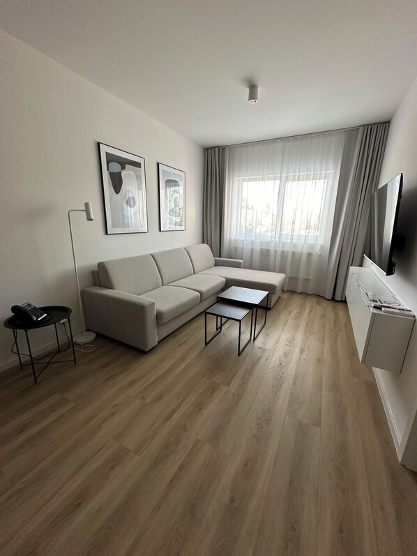 A modern living room with a sofa, two coffee tables, a flat-screen TV, and artwork on the wall.