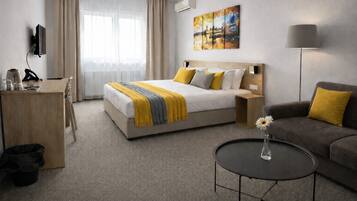 Una habitación de hotel con cama, escritorio, sofá, mesa de centro y un cuadro en la pared.