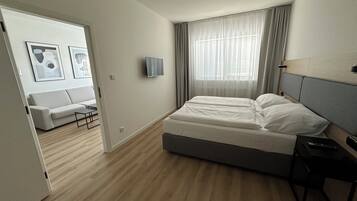 A modern bedroom with a large bed, a bedside table, a TV mounted on the wall, and a window with curtains.