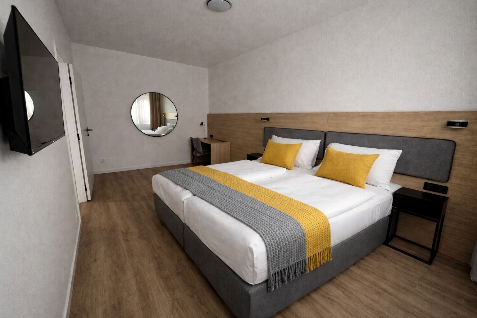 Ett modernt hotellrum med en stor säng, ett sängbord, en spegel och en sänggavel i trä.