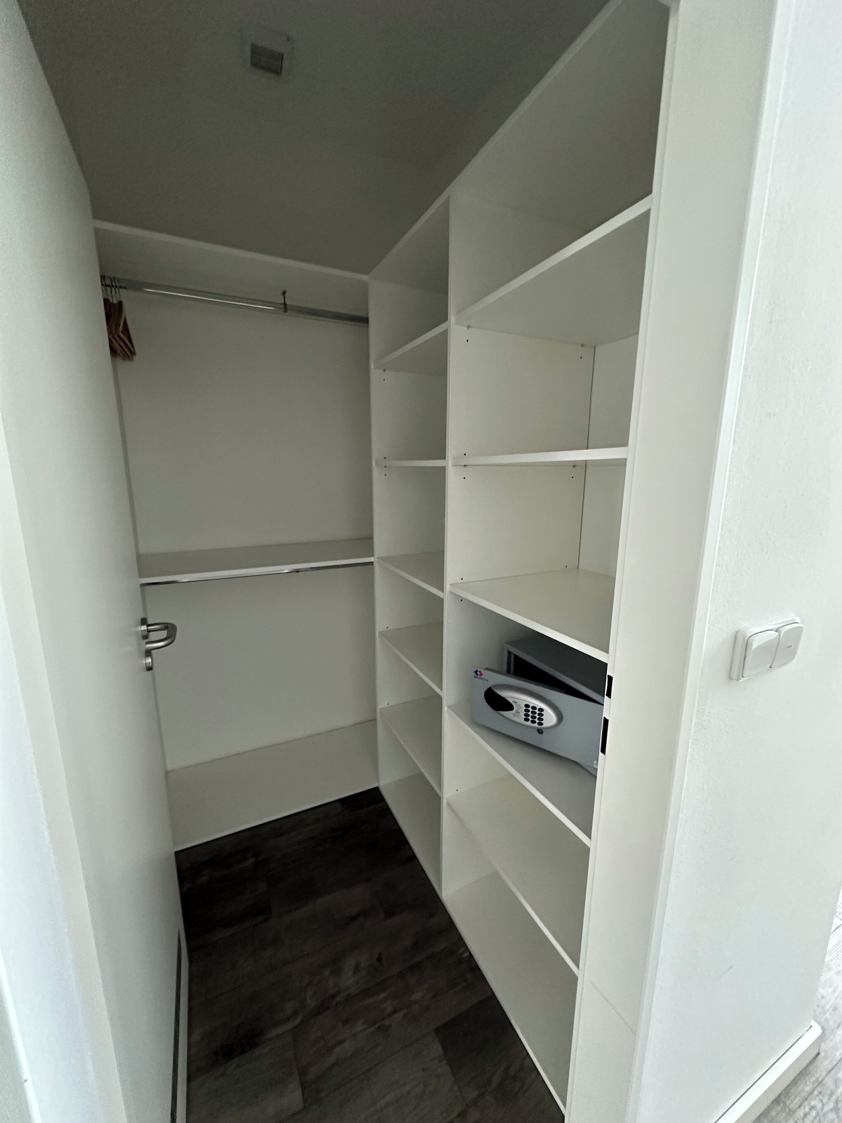 A walk-in closet with white shelving units and a dark wood floor.