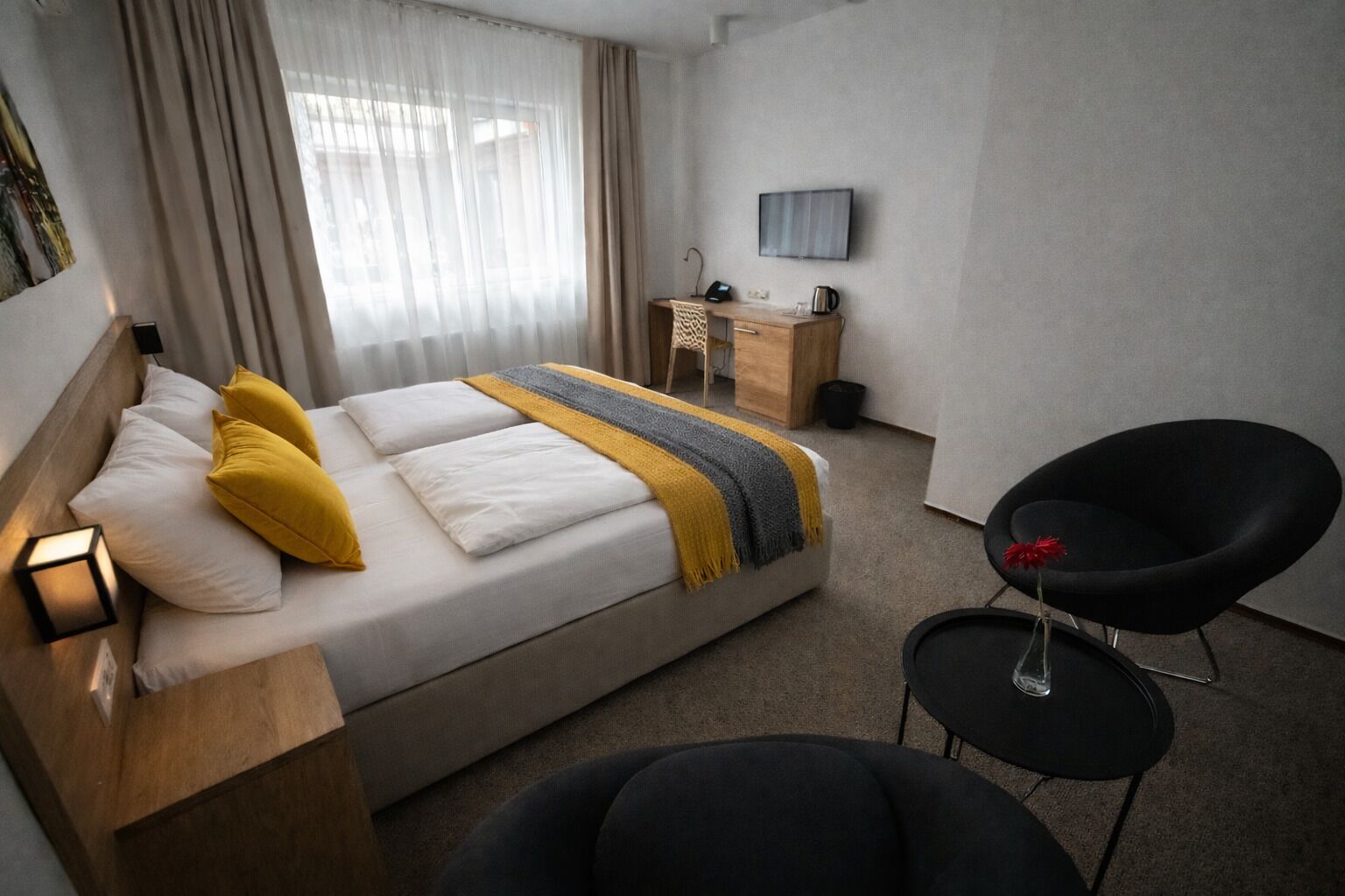 Habitació d'hotel amb llit, escriptori, cadira i televisió penjada a la paret.