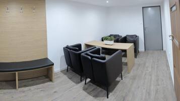 Une petite salle de réunion avec une table en bois, des chaises noires, une plante en pot et une porte au fond.