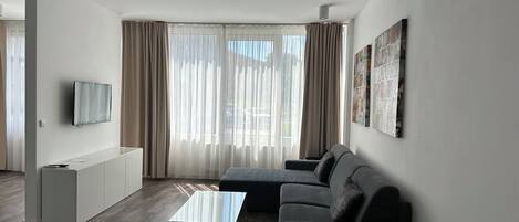 Una sala de estar moderna con un sofá, una mesa de centro, un televisor y un amplio ventanal con cortinas.