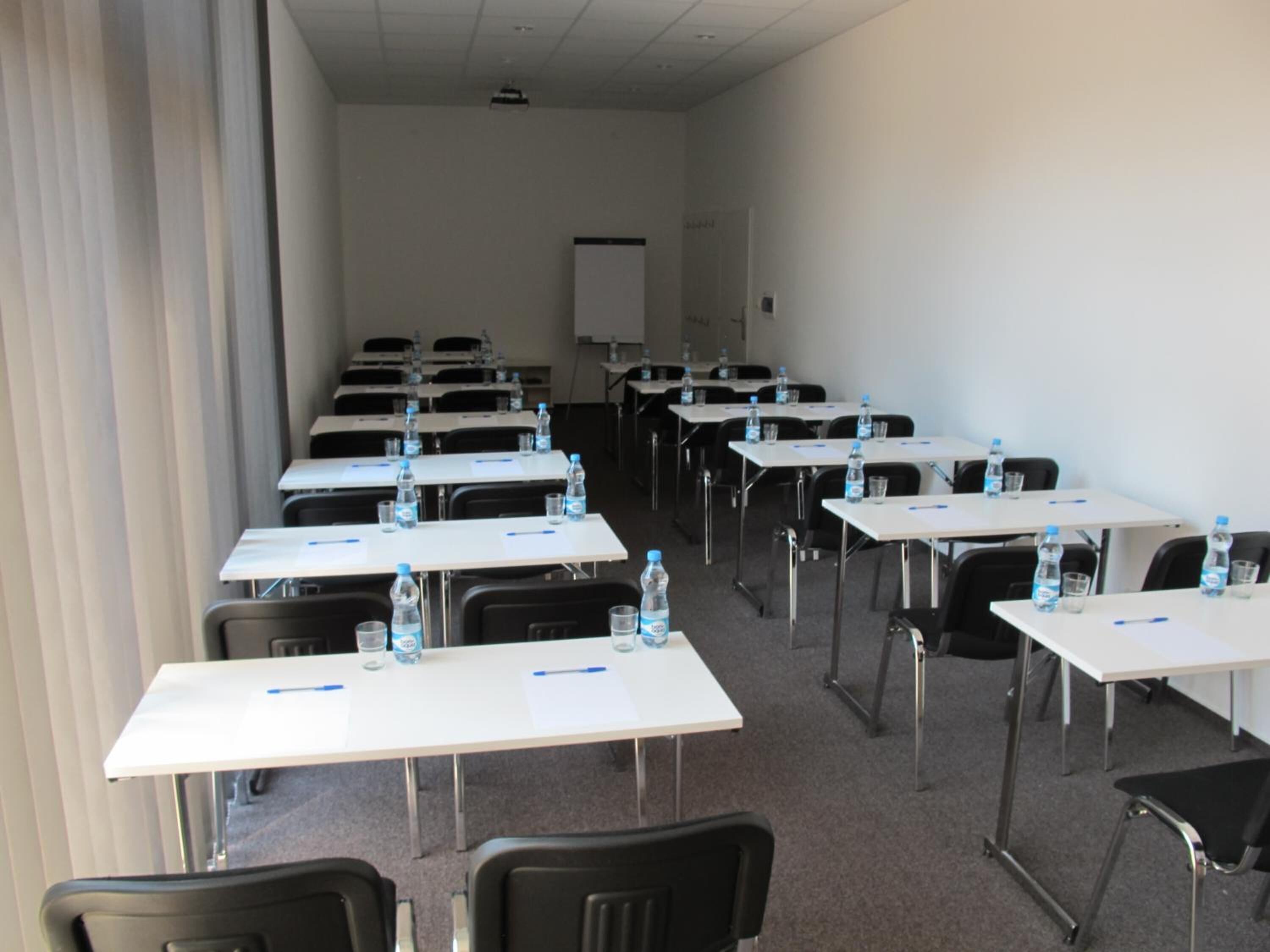 A conference room with rows of tables and chairs, each with a water bottle and a pen.