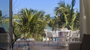 A sunlit outdoor seating area with a table and chairs, surrounded by palm trees and overlooking a pool. - Ultravioleta Boutique Residences (Cabarete)