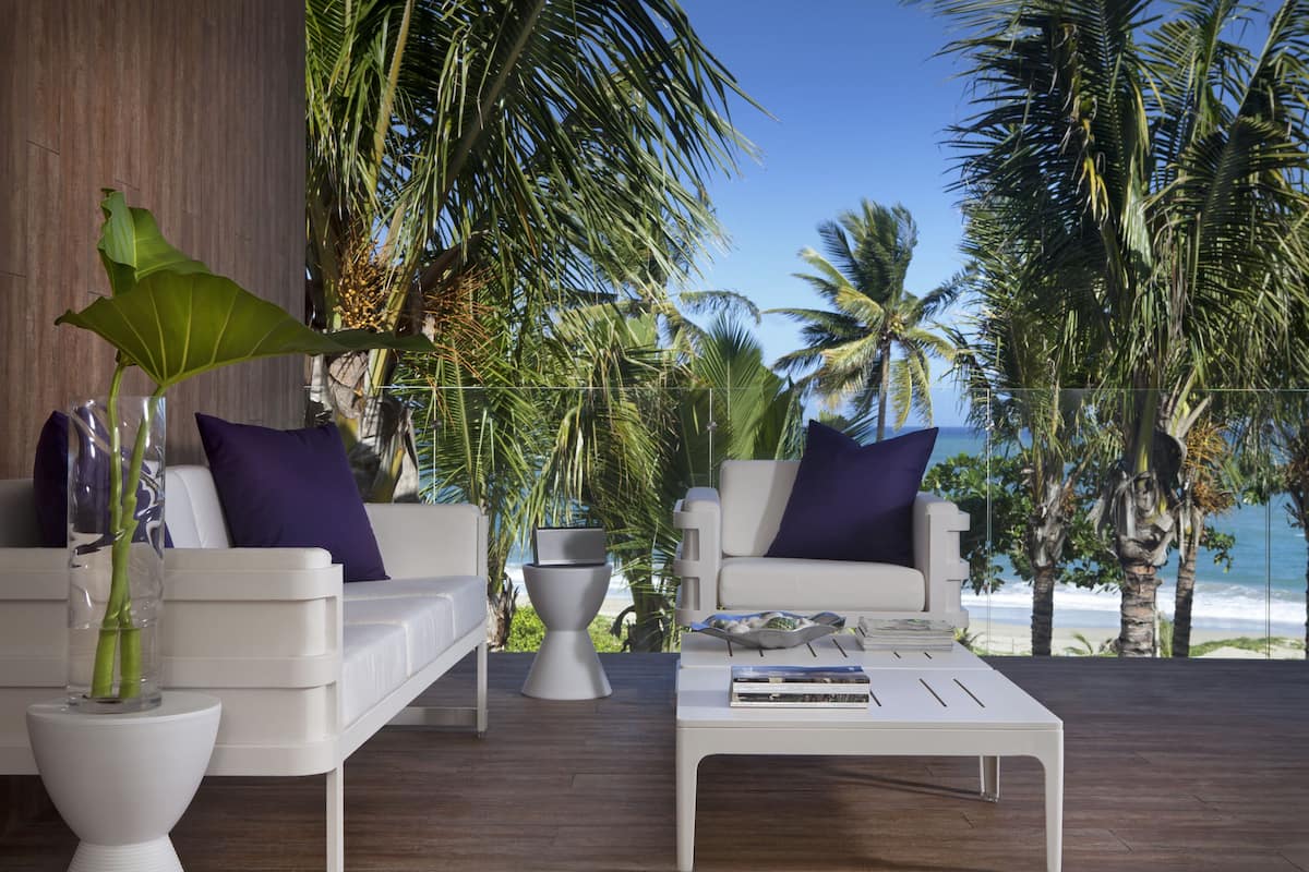 A modern outdoor seating area with white sofas and purple cushions, a coffee table, and a large plant.