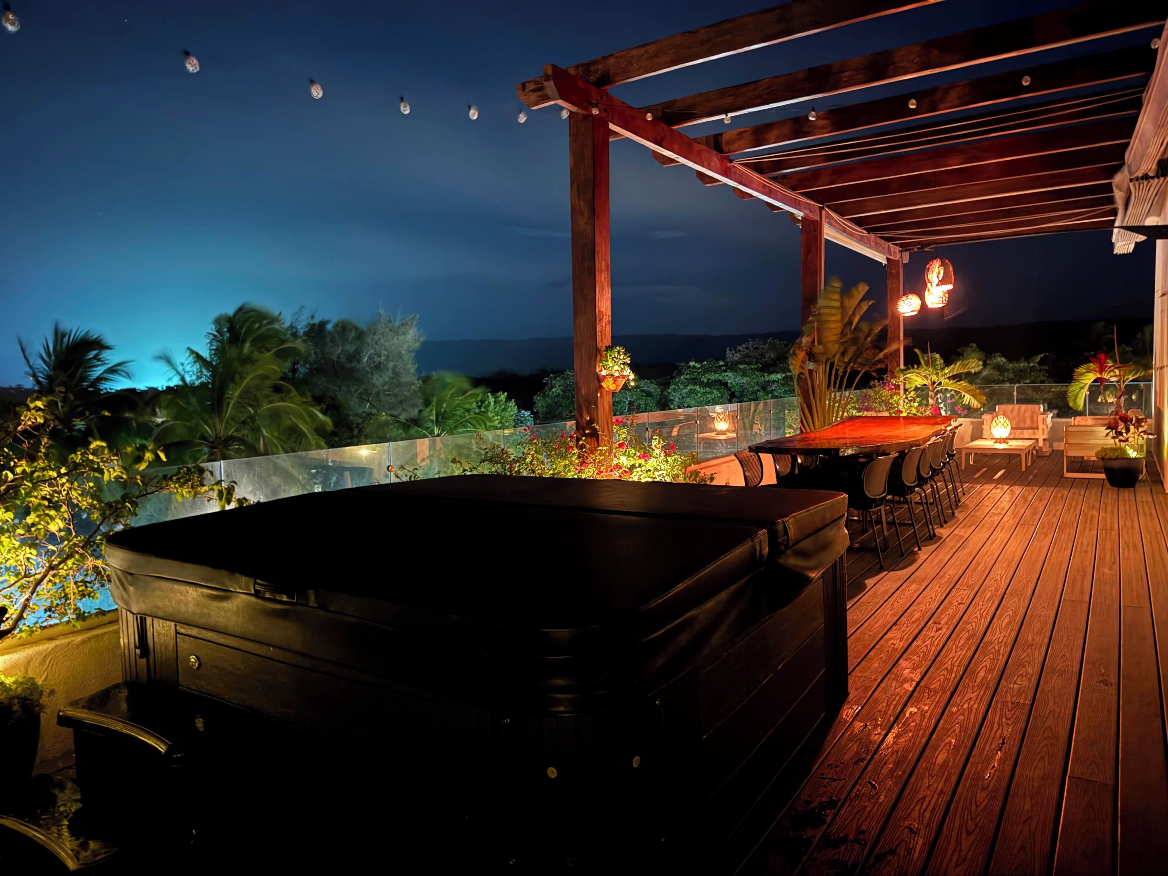 Terraza de madera con jacuzzi, asientos al aire libre y luces colgantes.