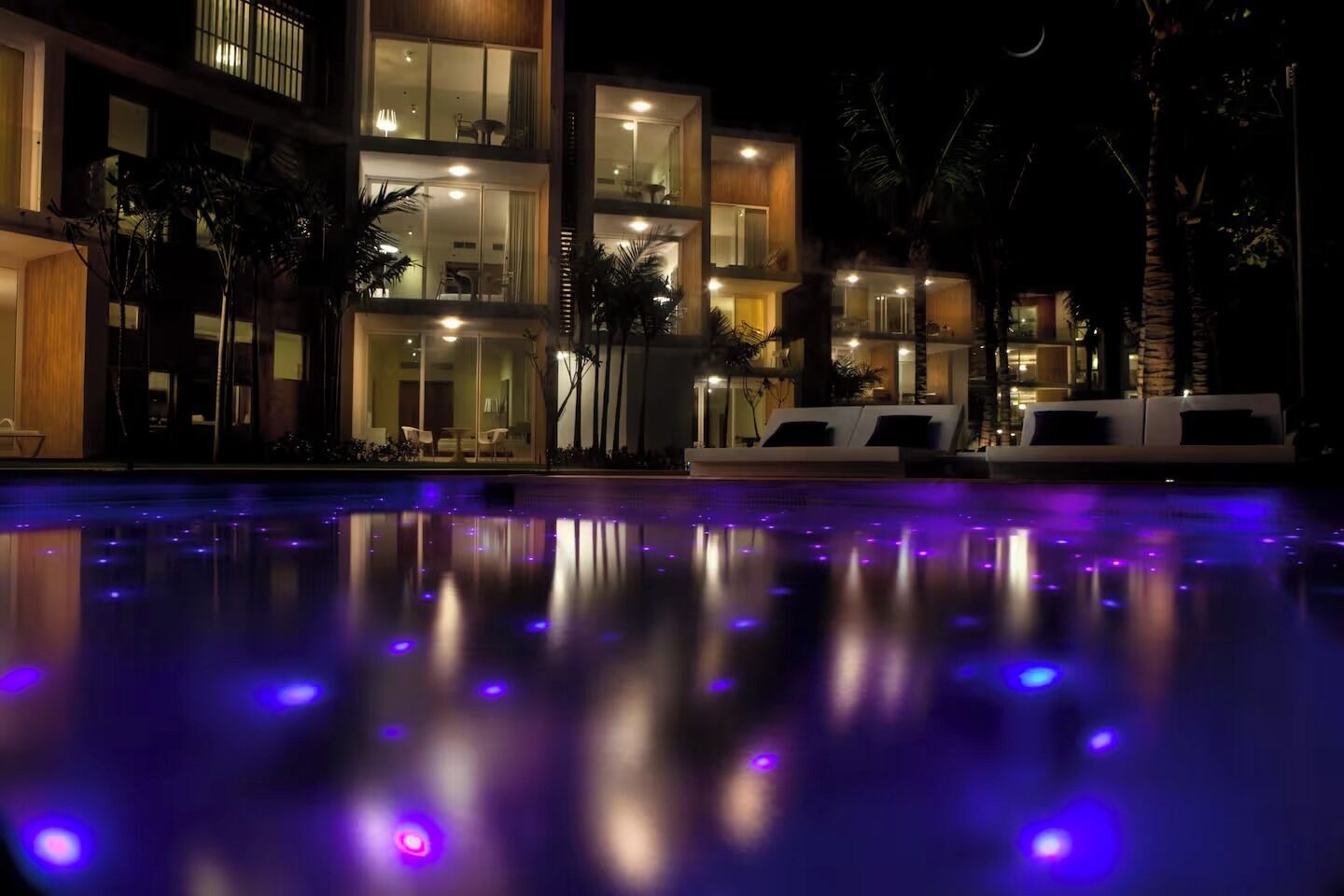 A multi-story hotel with a swimming pool at night, illuminated by purple lights.