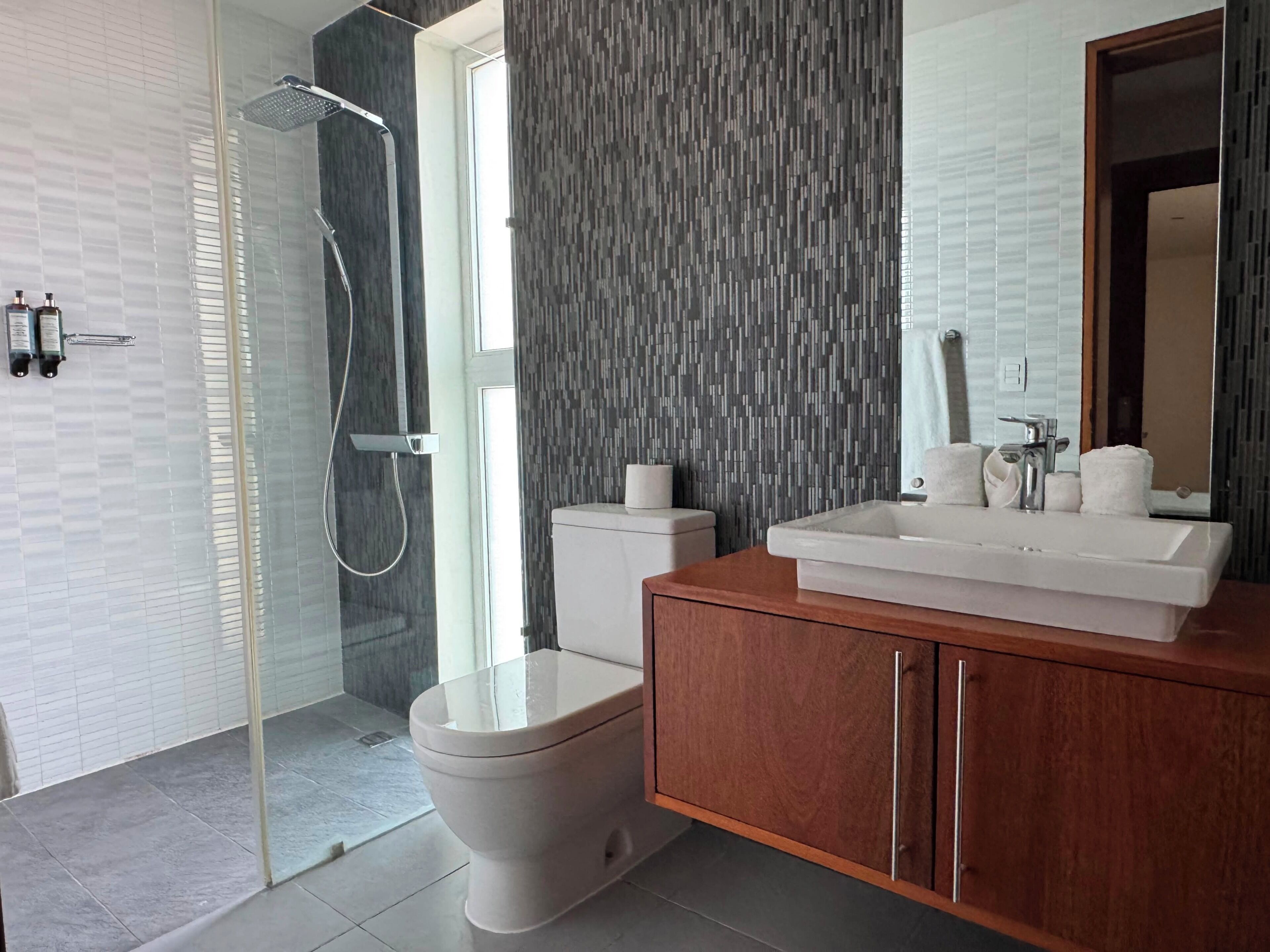 A modern bathroom with a glass shower enclosure, a toilet, a vanity with a sink, and a mirror.