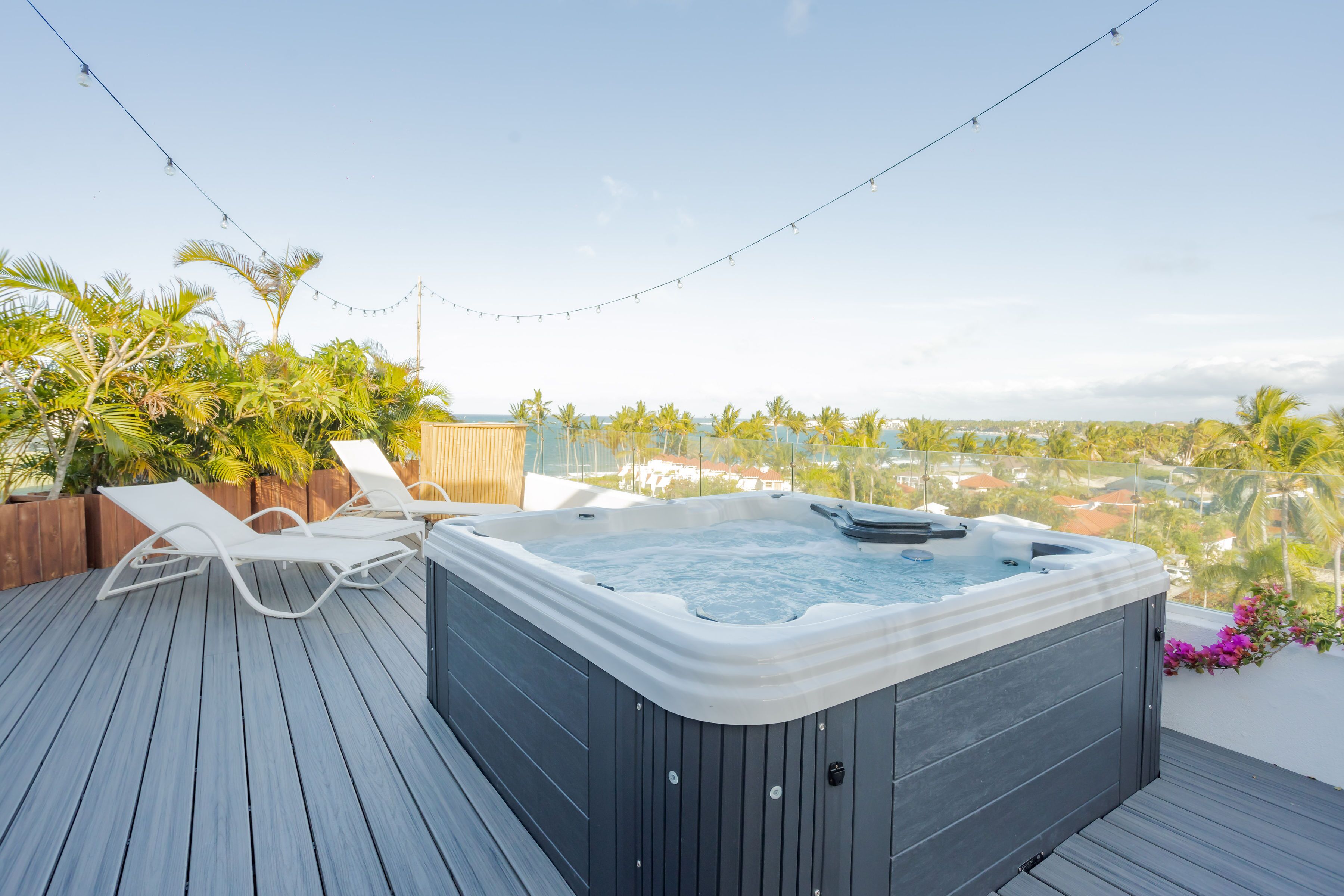 Un bain à remous sur une terrasse en bois, agrémentée de chaises longues, entouré de verdure et offrant une vue sur le paysage urbain.