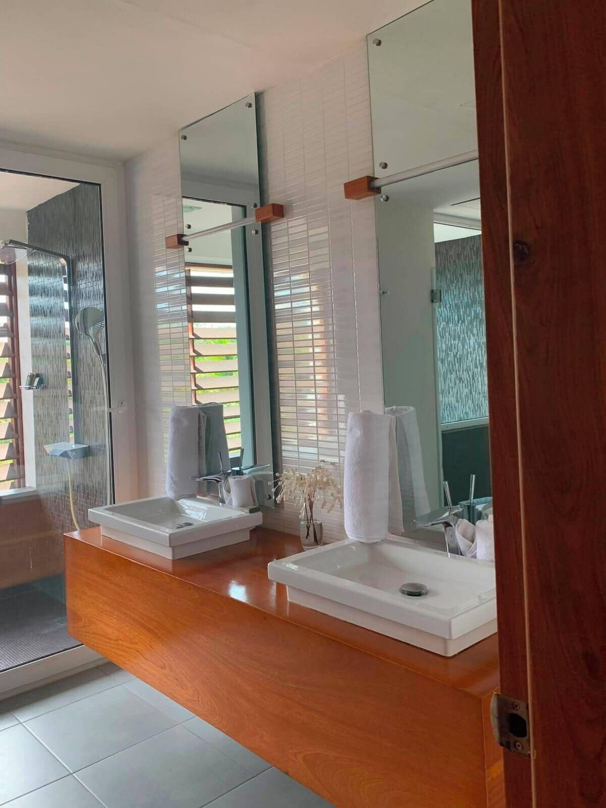 A modern bathroom with two sinks, a shower, and large mirrors.