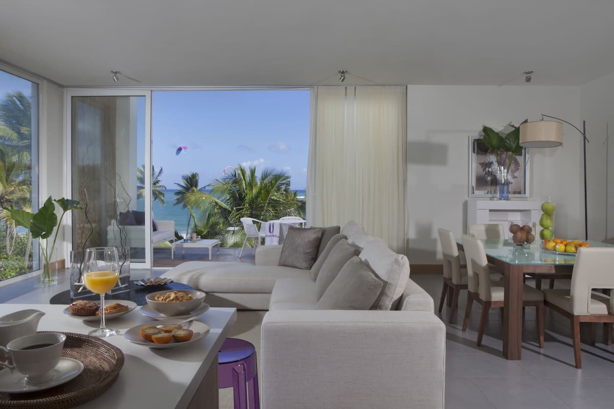 A modern living room with a glass dining table, a sofa, and a view of the ocean.