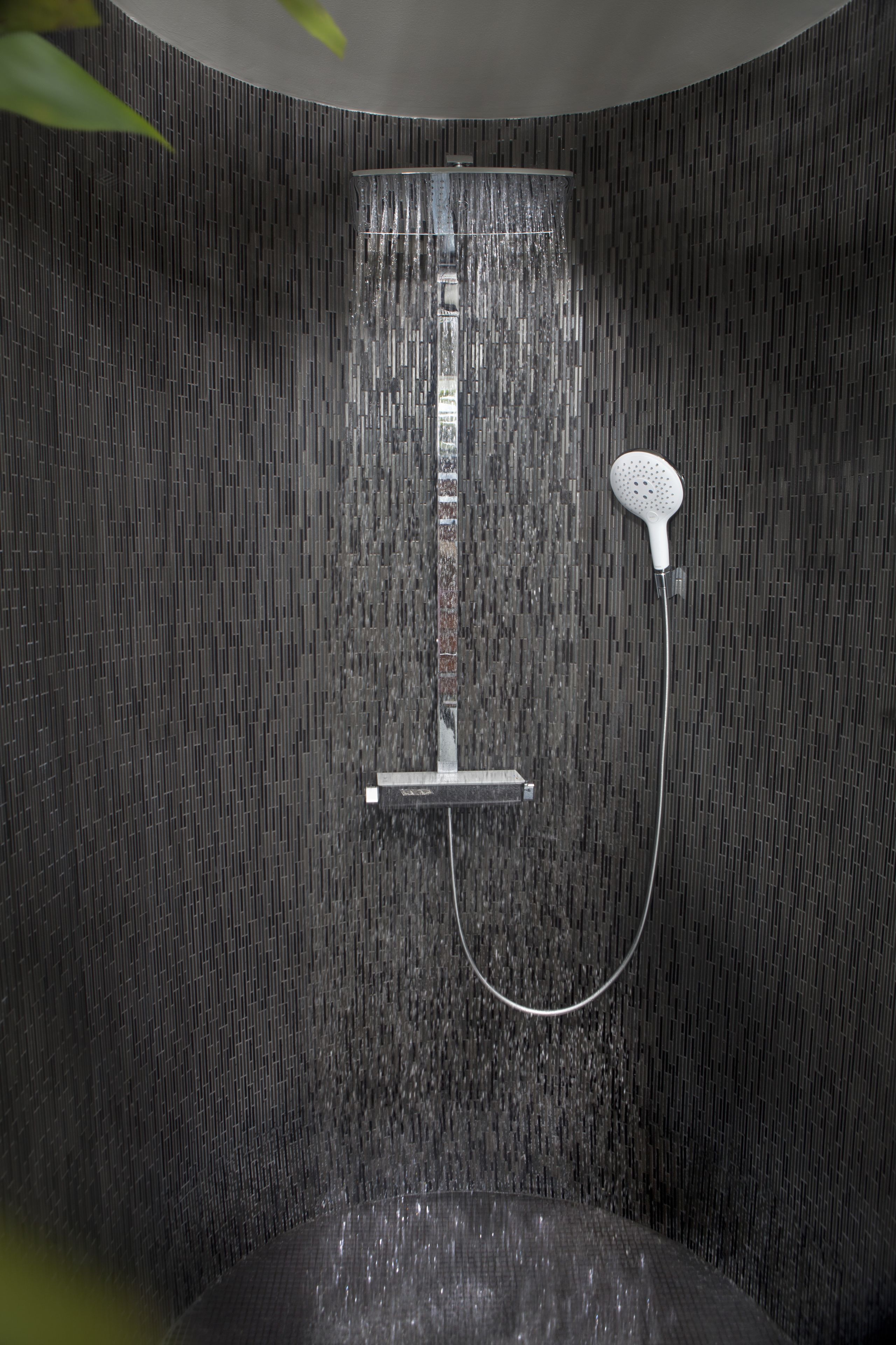 A shower with a handheld showerhead and a wall-mounted control panel.