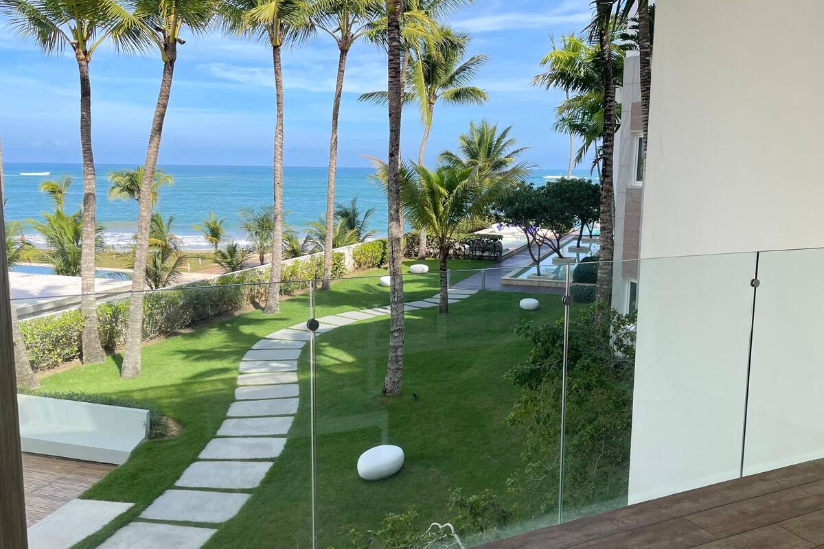 A balcony with a view of the ocean, palm trees, and a stone pathway.