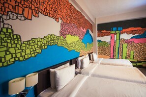 Una habitación de hotel con dos camas, un mural abstracto grande en la pared y una mesita de noche con una lámpara.