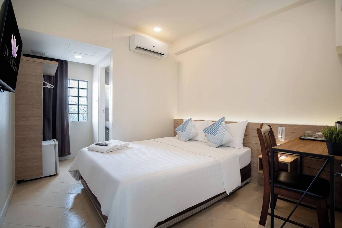 Une chambre d’hôtel équipée d’un lit, d’un bureau, d’une chaise, d’un climatiseur et d’une fenêtre.