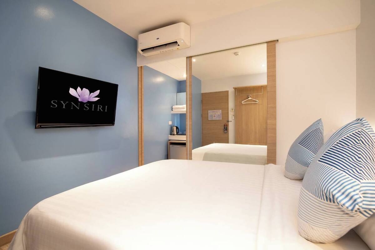 Une chambre d’hôtel avec un lit, un téléviseur fixé au mur et une armoire en bois.