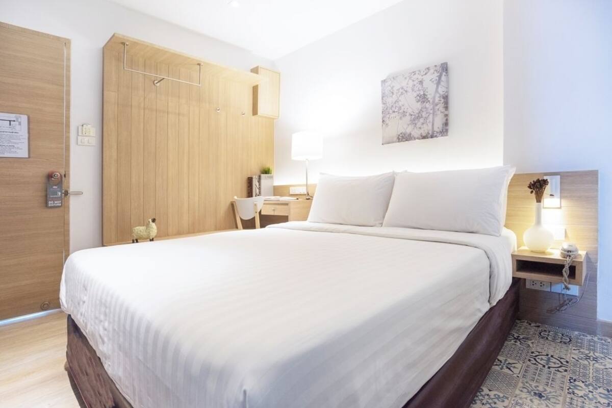 Une chambre d’hôtel avec un lit, une table de chevet, une lampe et une armoire en bois.
