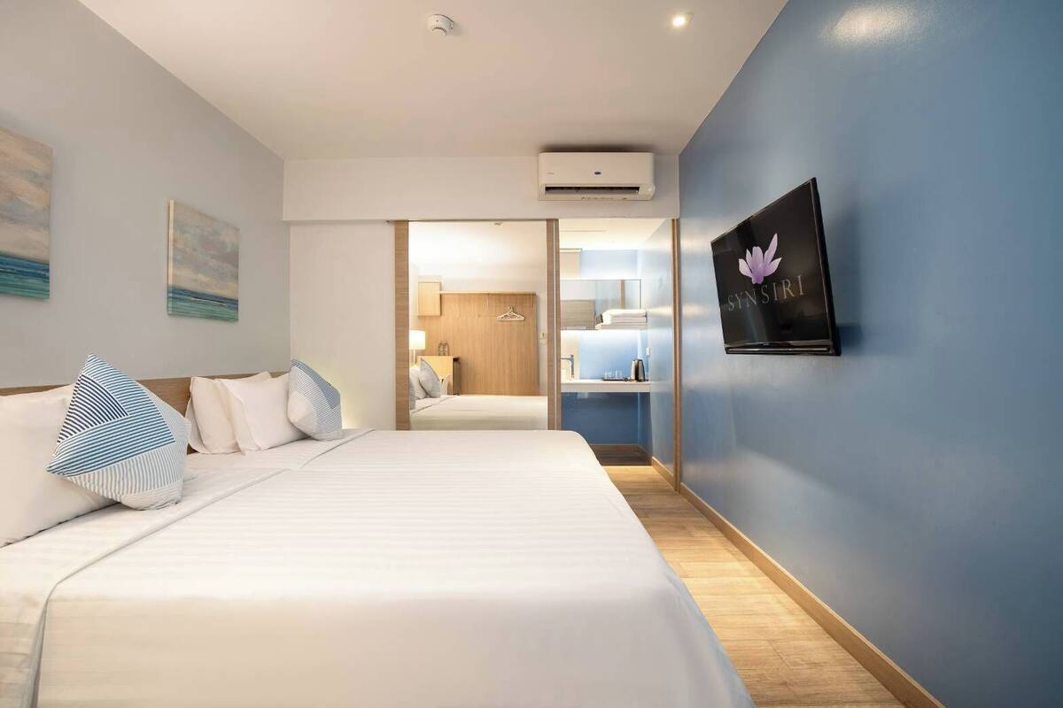 Une chambre d’hôtel avec un grand lit, un téléviseur à écran plat fixé au mur et une salle de bain visible à travers une porte ouverte.