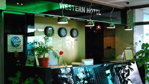 Uma receção com um relógio, uma planta e a placa do Hotel Western.
