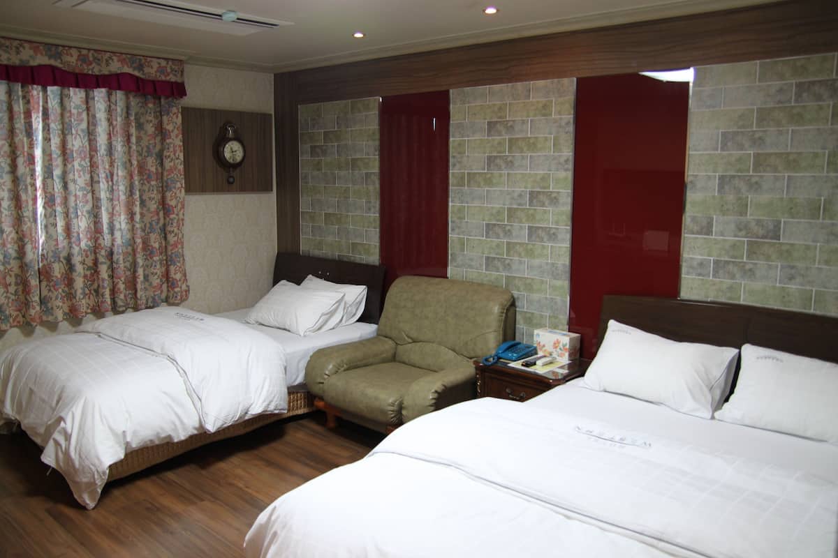 A hotel room with two beds, a chair, a nightstand, and a clock on the wall.