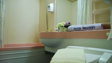 A bathroom with a bathtub, a toilet, a sink, and a mirror. There are towels with "HOTEL WESTERN" written on them.