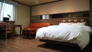 Quarto de hotel com uma cama grande, uma escrivaninha com computador, uma cadeira e uma mesinha.