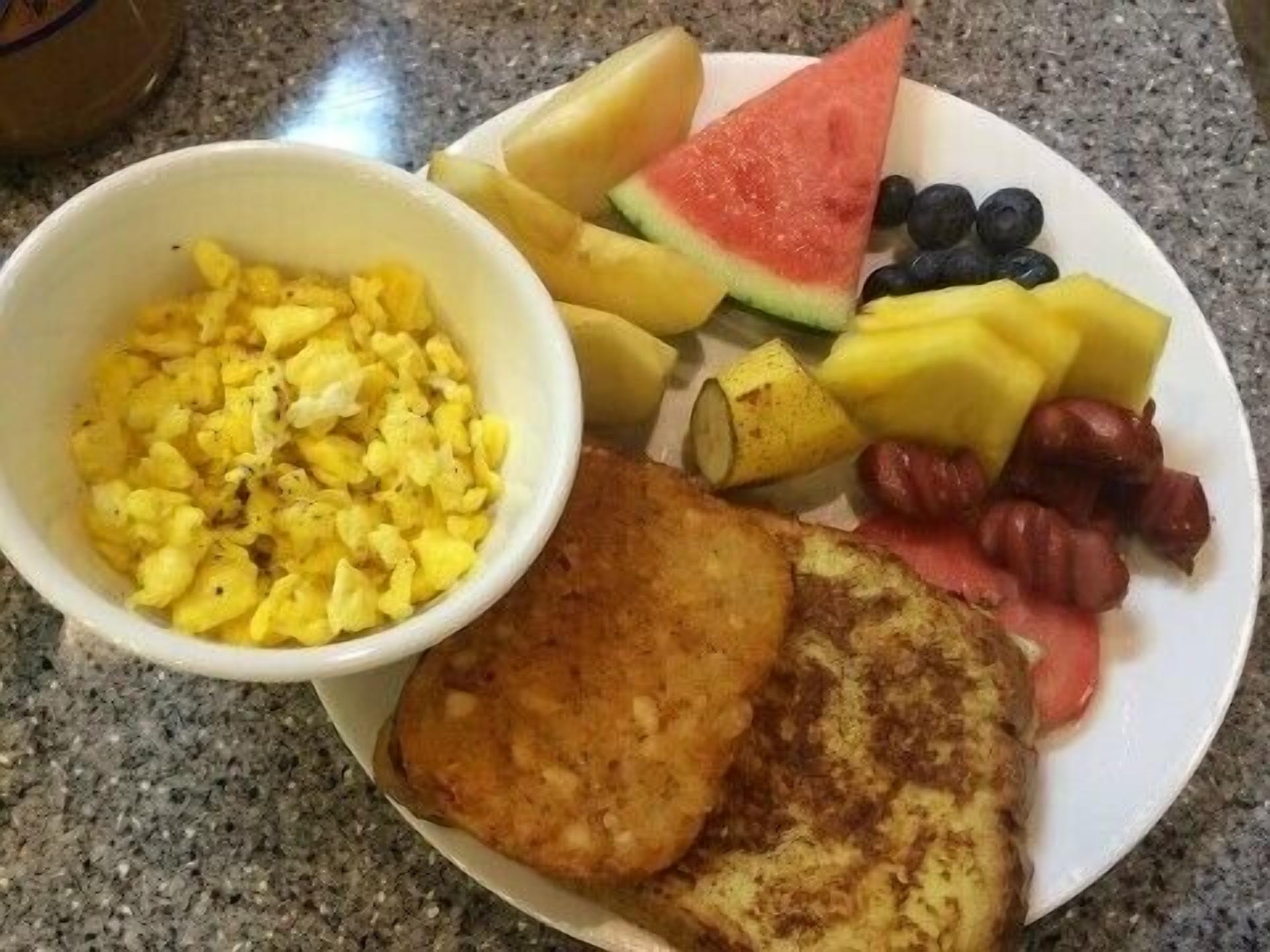 A plate with scrambled eggs, toast, watermelon, mango, blueberries, pineapple chunks, and red grapes.
