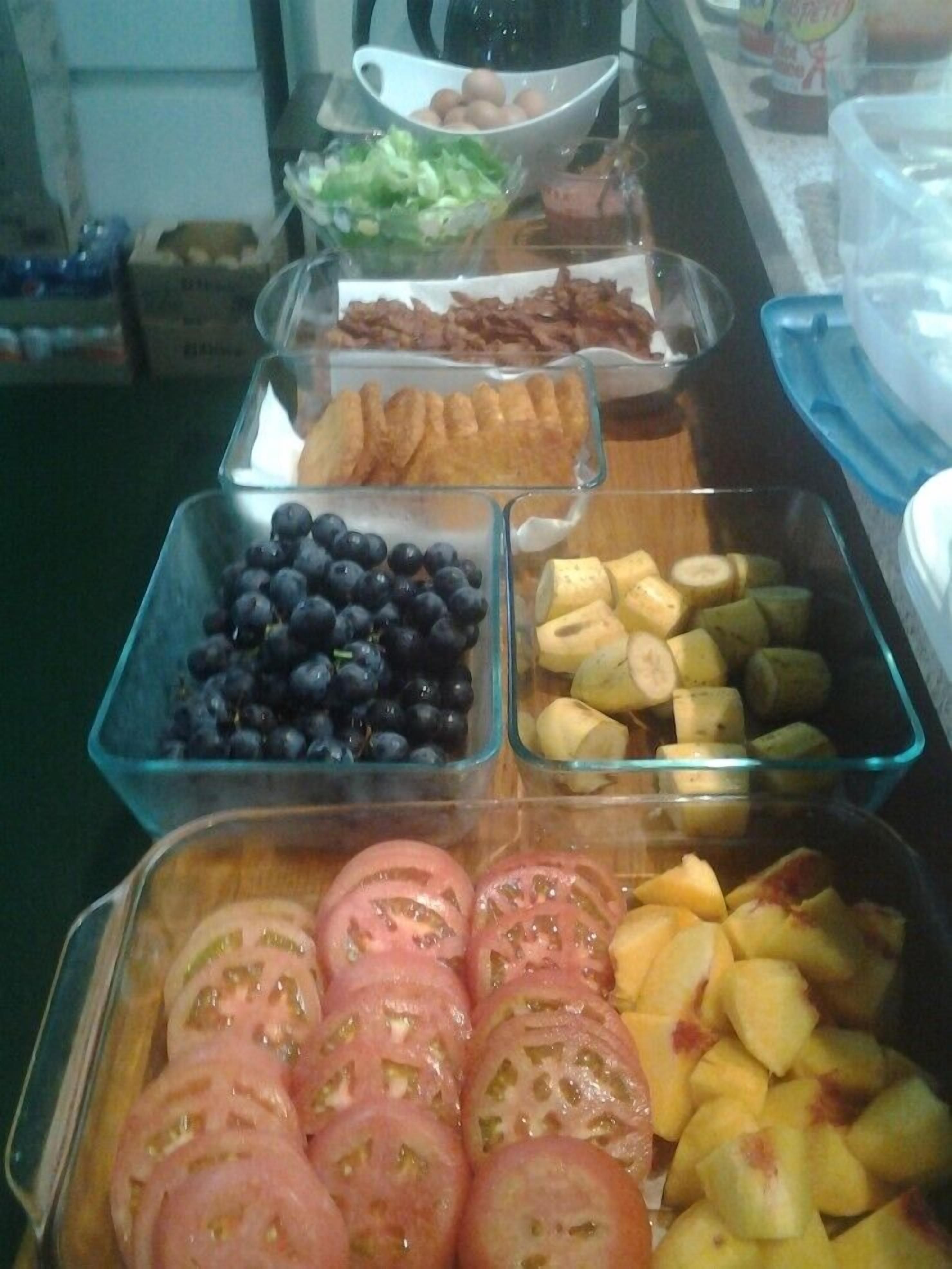 Un bufé con diversos alimentos, incluyendo uvas, plátanos, tomates y otras frutas.