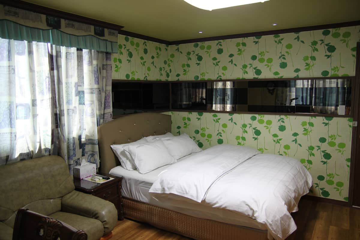 A bedroom with a large bed, a nightstand, a chair, and a wall-mounted TV.