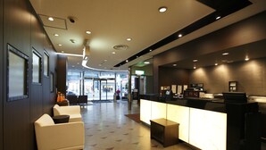 A modern hotel lobby with a reception desk, seating area, and a view of the street.