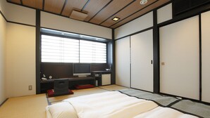 A traditional Japanese-style bedroom with tatami flooring, a futon bed, a television, and sliding doors.