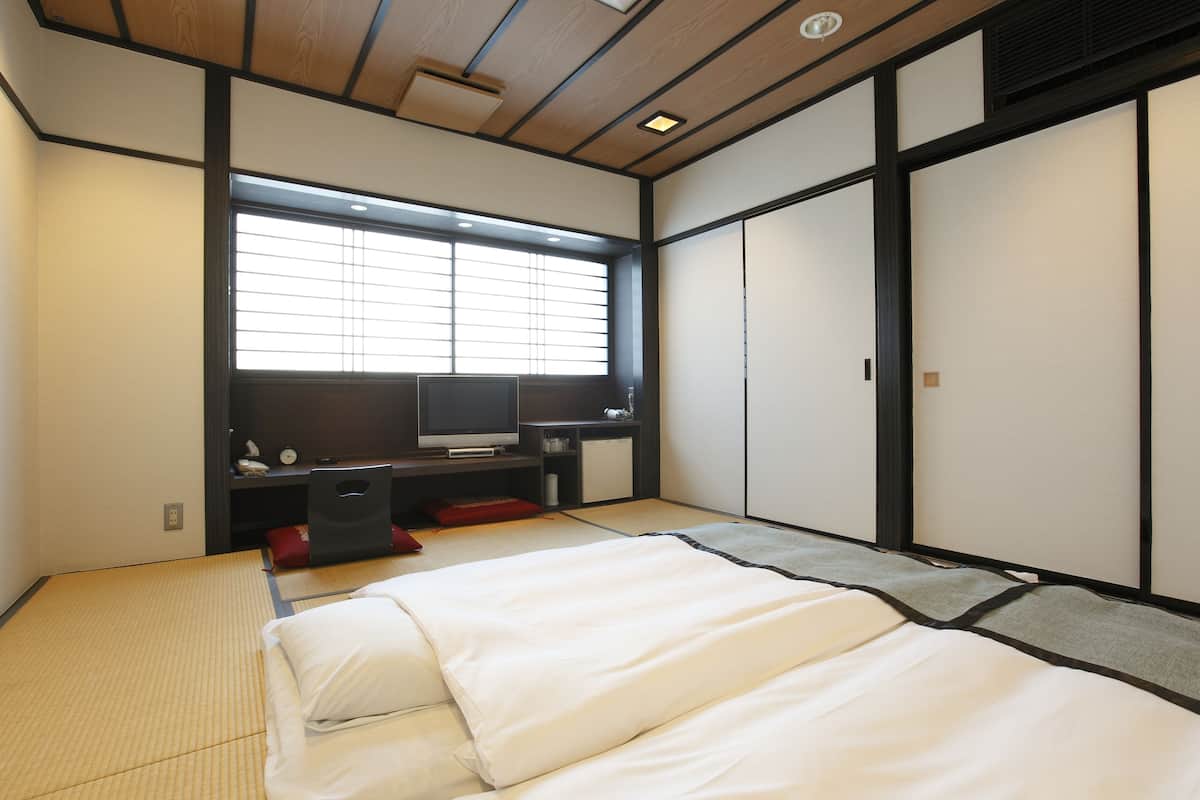 A traditional Japanese-style bedroom with tatami flooring, a futon bed, a television, and sliding doors.