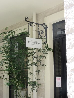 A sign for Café et Restaurant Jeu de Paume Takajo, with a hanging sign and a staff notice on a building facade.