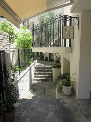 A stone staircase leading to a second floor with a balcony, surrounded by potted plants and a brick wall.