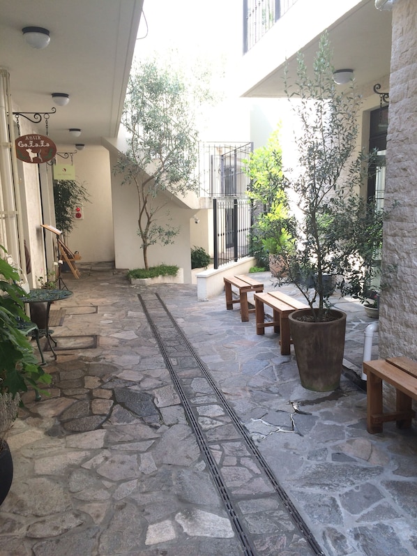 A courtyard with stone flooring, wooden benches, potted plants, and a sign for a restaurant.
