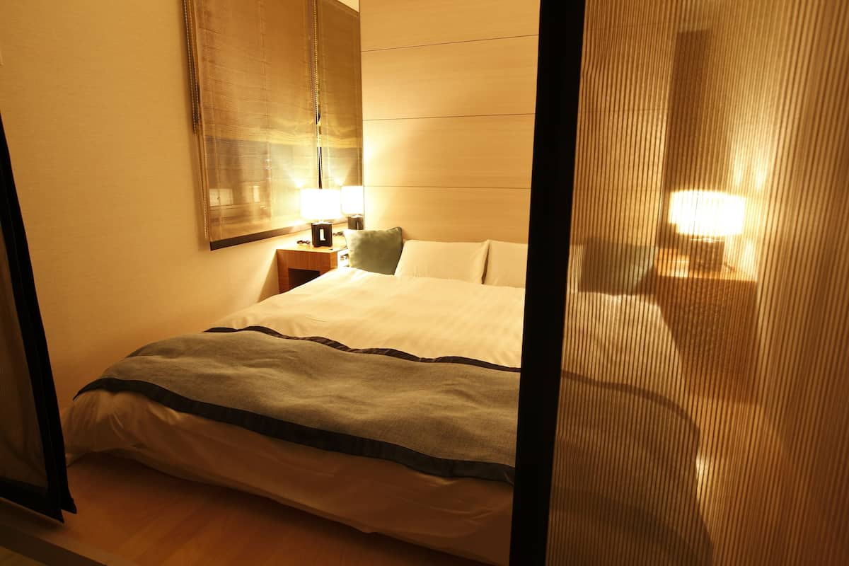 A hotel room with a bed, a nightstand, a lamp, and a mirror.