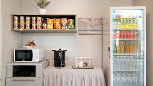 Een kitchenette met een magnetron, een kleine koelkast, een plank vol conserven en een koelkast gevuld met drankjes.