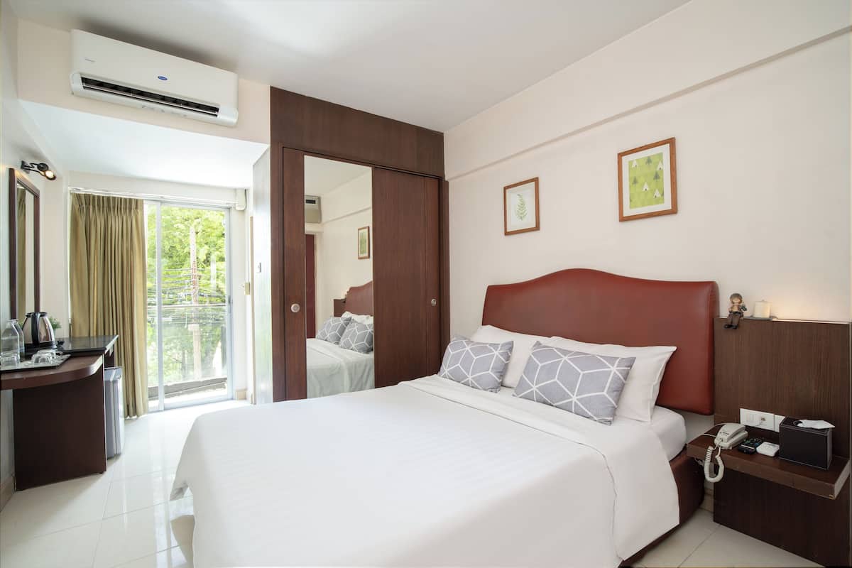 A hotel room with a bed, a desk with a telephone, and a window with curtains.