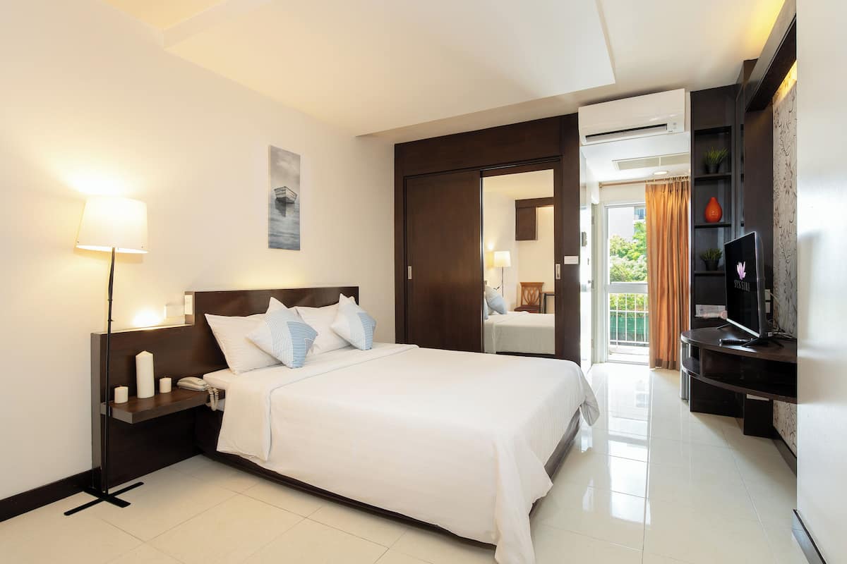 A hotel room with a bed, bedside table, lamp, TV, and a view of the outside.