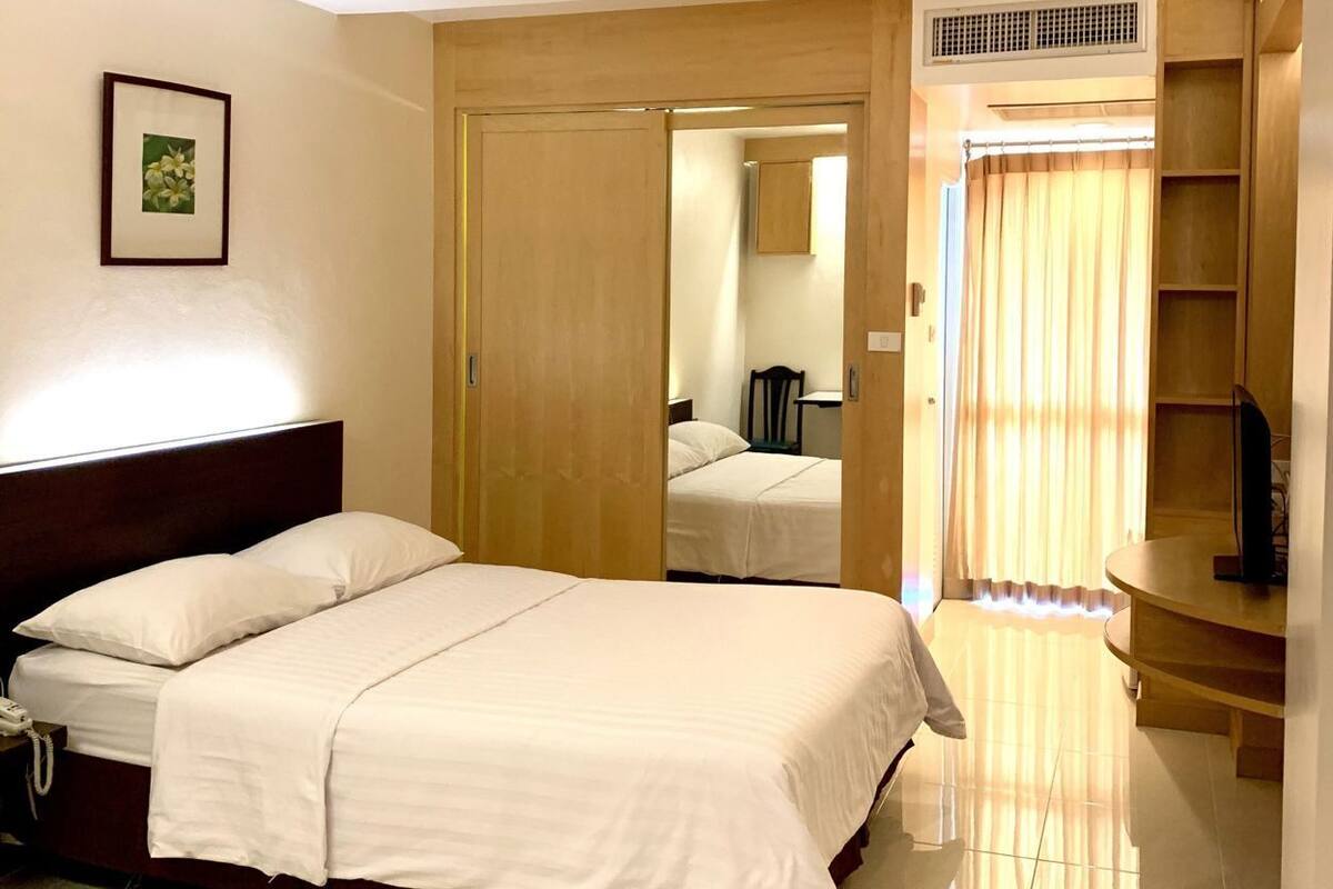 A hotel room with a bed, a bedside table with a phone, a mirror, a wardrobe, and a TV stand.