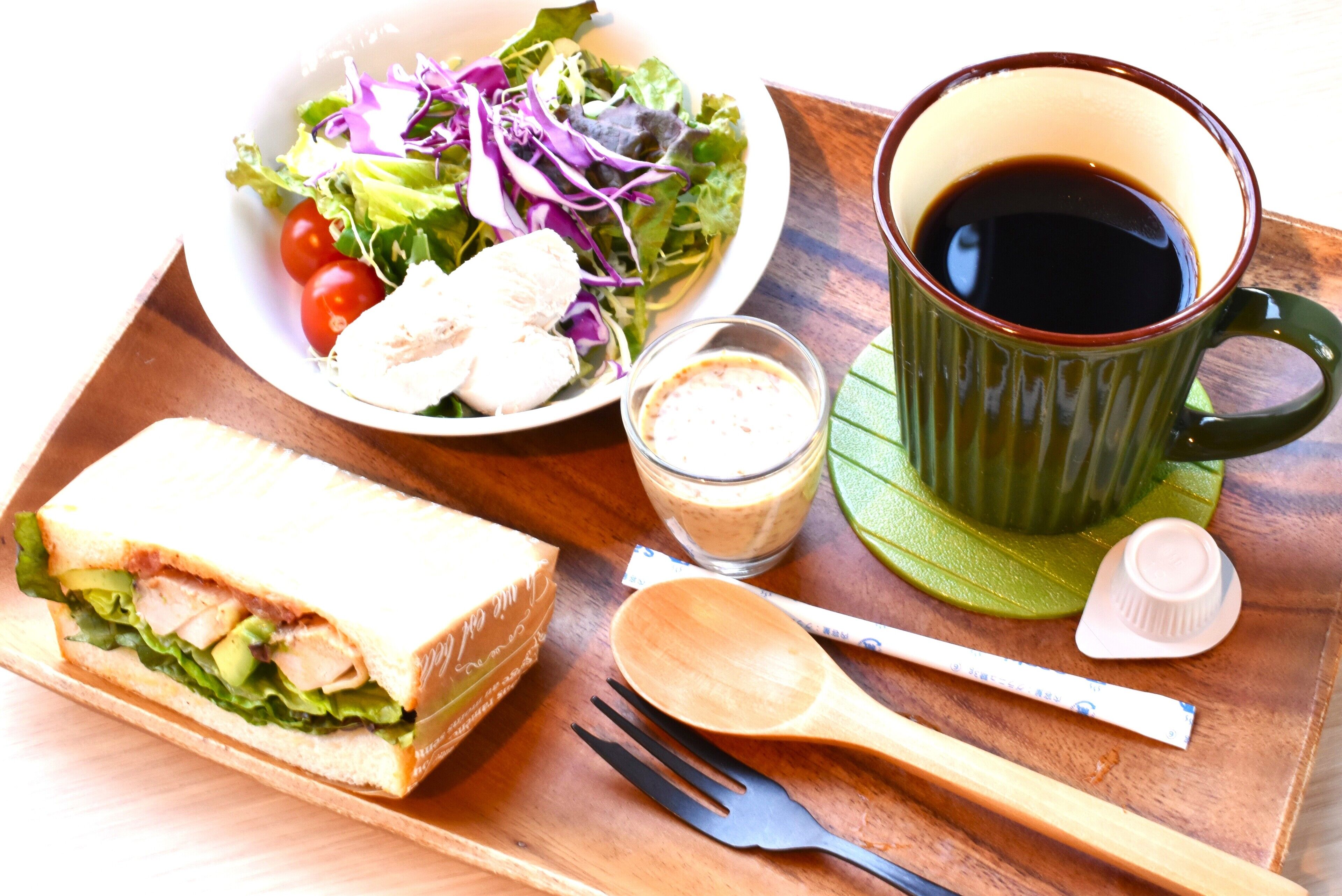 A meal tray with a sandwich, salad, cup of coffee, and a spoon.