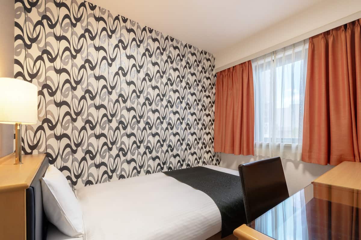 Une chambre d’hôtel avec un papier peint à motifs, un lit, un bureau avec un ordinateur portable, une télévision et une fenêtre avec des rideaux.