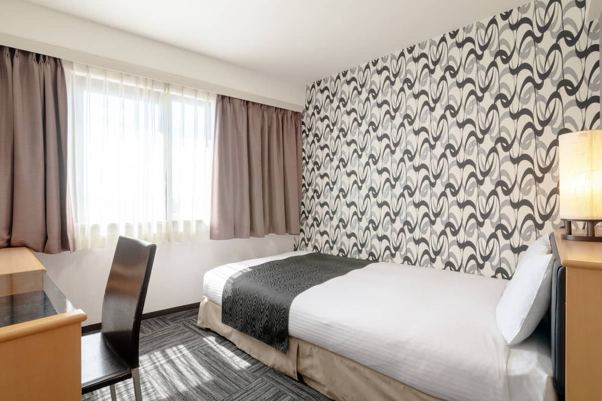 Une chambre d’hôtel avec un lit, un bureau, une chaise, une télévision et un mur décoré d’un motif.