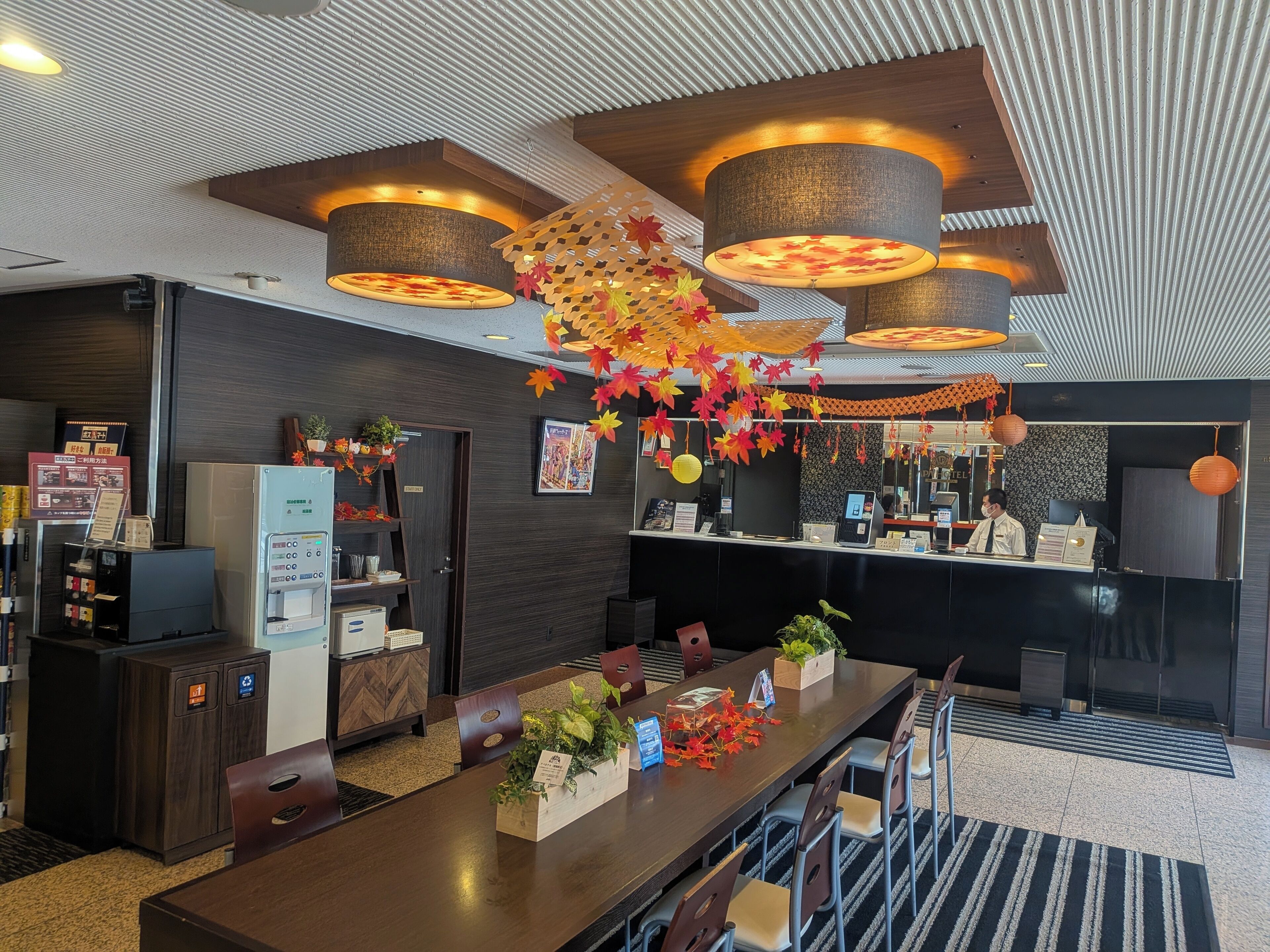 A hotel lobby with a reception desk, seating area, and a large wooden table with plants.